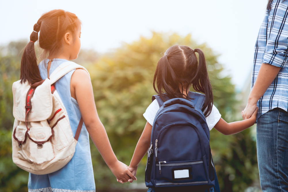 Two children holding their parent's hand with backpacks on
